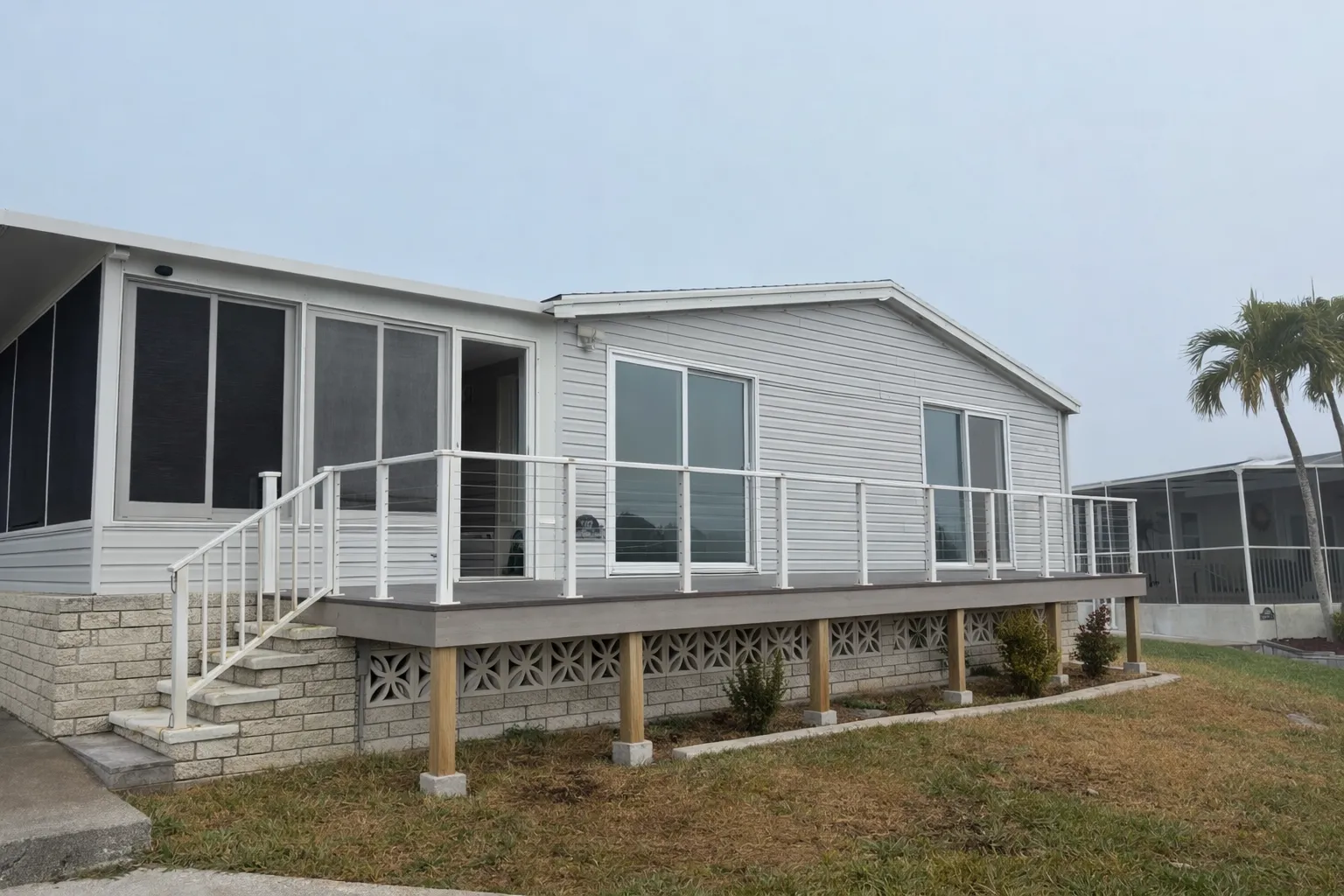 A deck with white cable railing and lattice skirting along a screened home