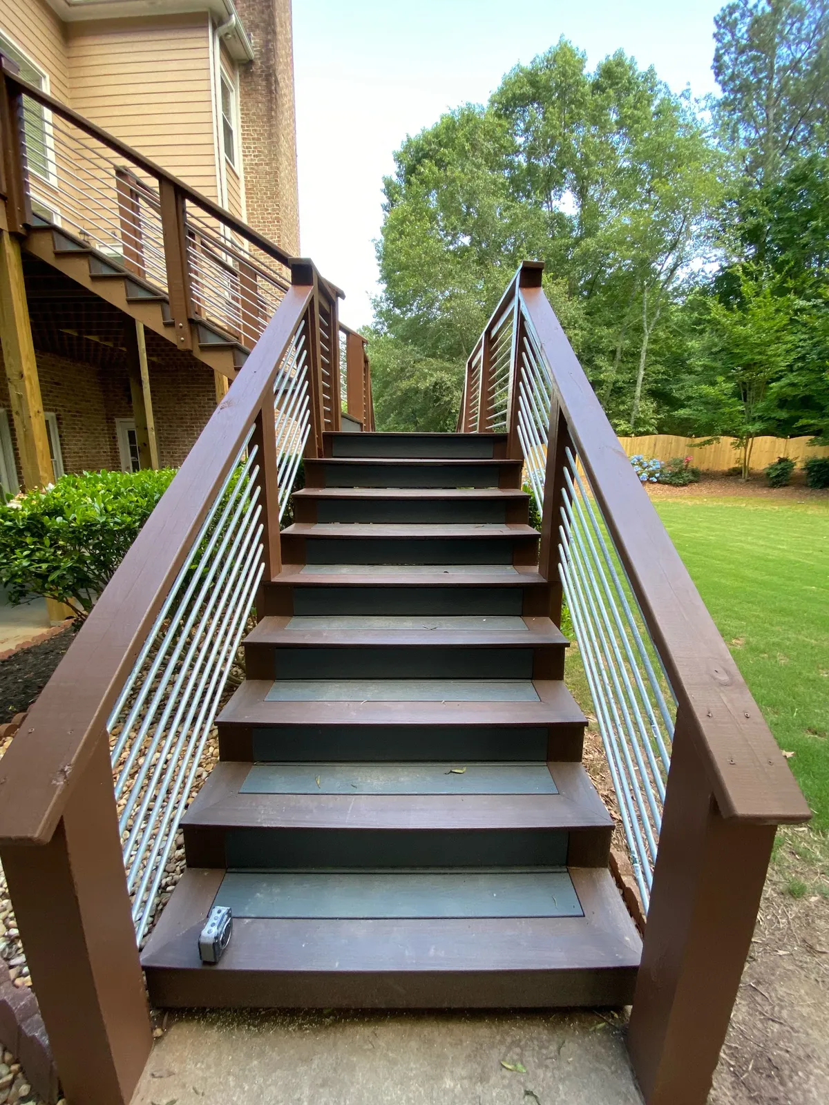 Dark-stained deck stairs with a wood-topped cable railing running down to a lawn