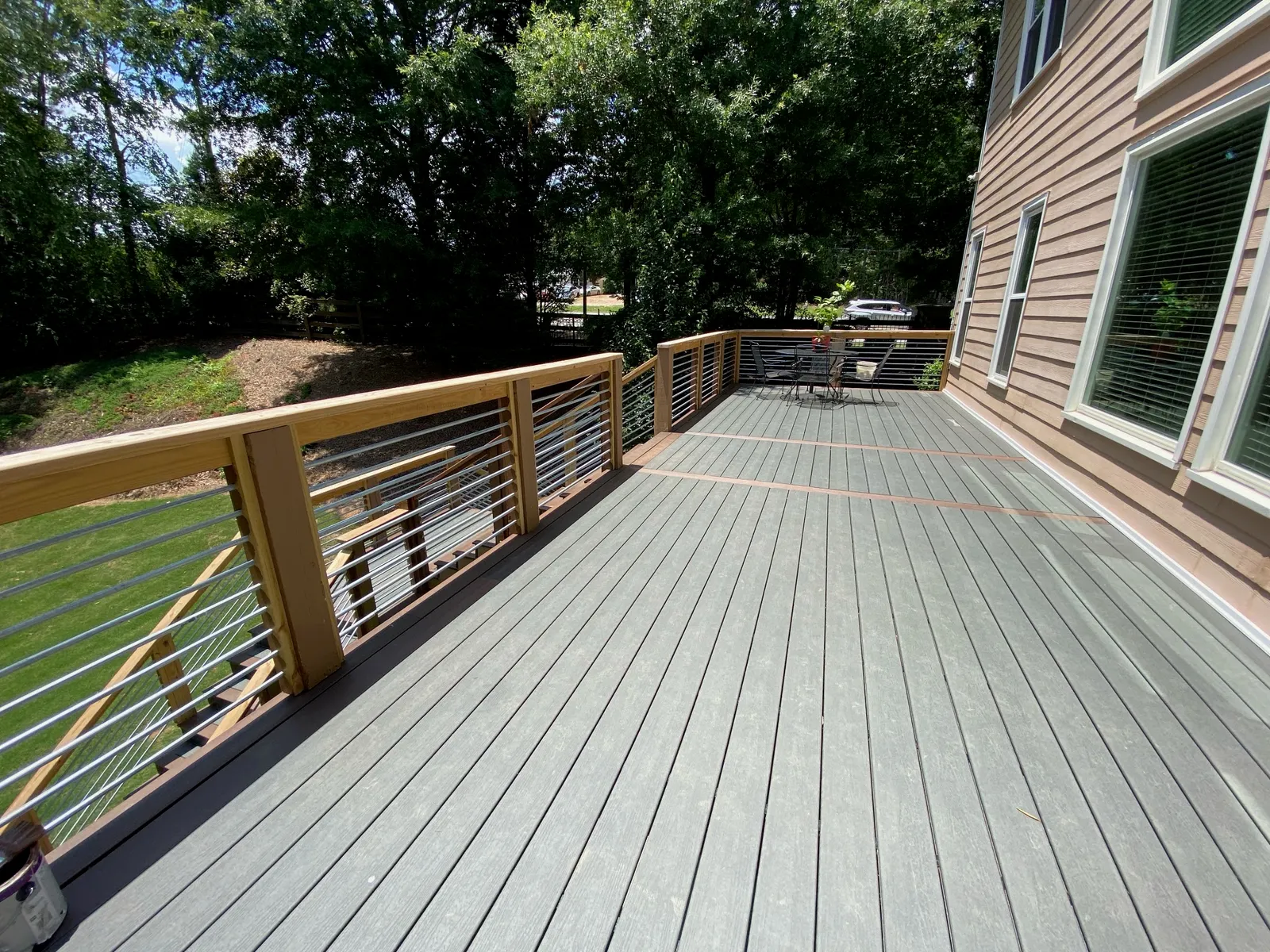 A wraparound composite deck with cable railing along a wood-sided house